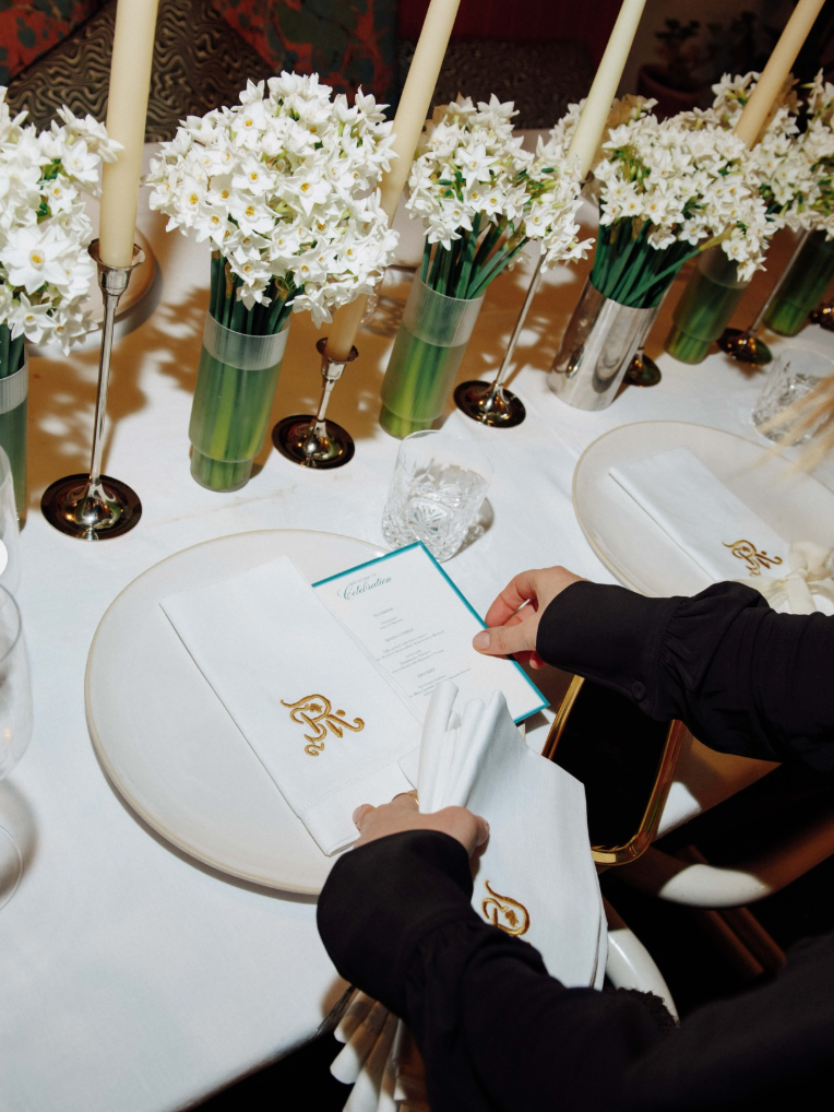 Person setting up a table with white flowers and place cards in a formal setting.