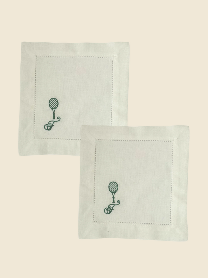 Two white  cocktail napkins with green embroidered designs on a white background